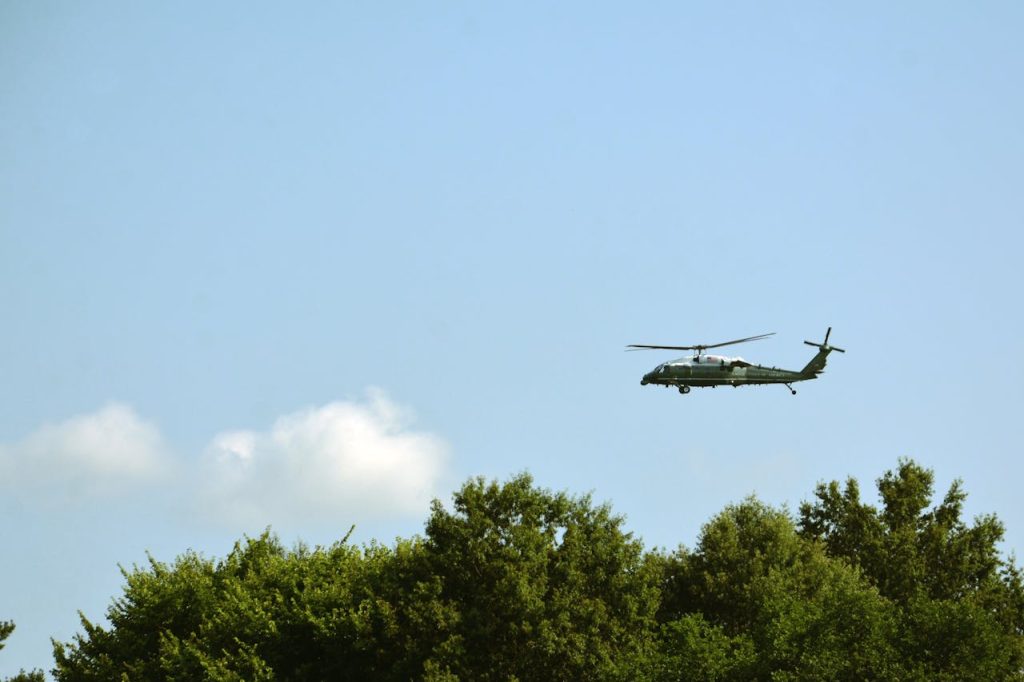 Utility helicopter flying high above green trees in Washington, DC under a clear sky.