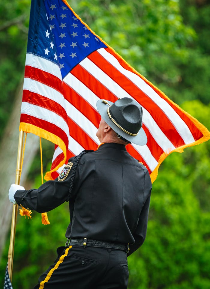 Military officer holding the American flag with vibrant greenery in the background.